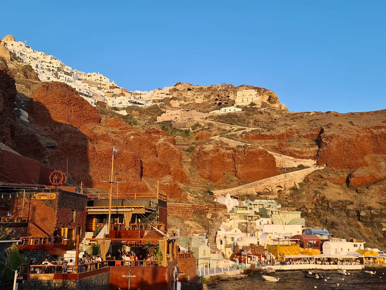 Tabernas del puerto de Amoudi Bay bajo los acantilados rojos, con Oia en lo alto