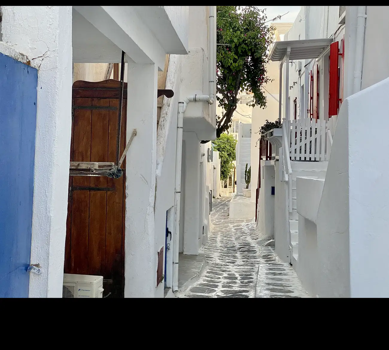 Callejuela de cantos rodados en la Chora de Mykonos con puertas de madera y balcones blancos