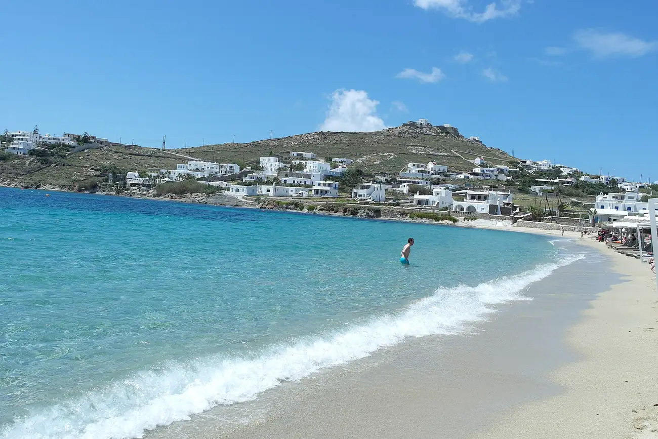Playa de Ornos en Mykonos con arena clara, agua turquesa y el pueblo detrás