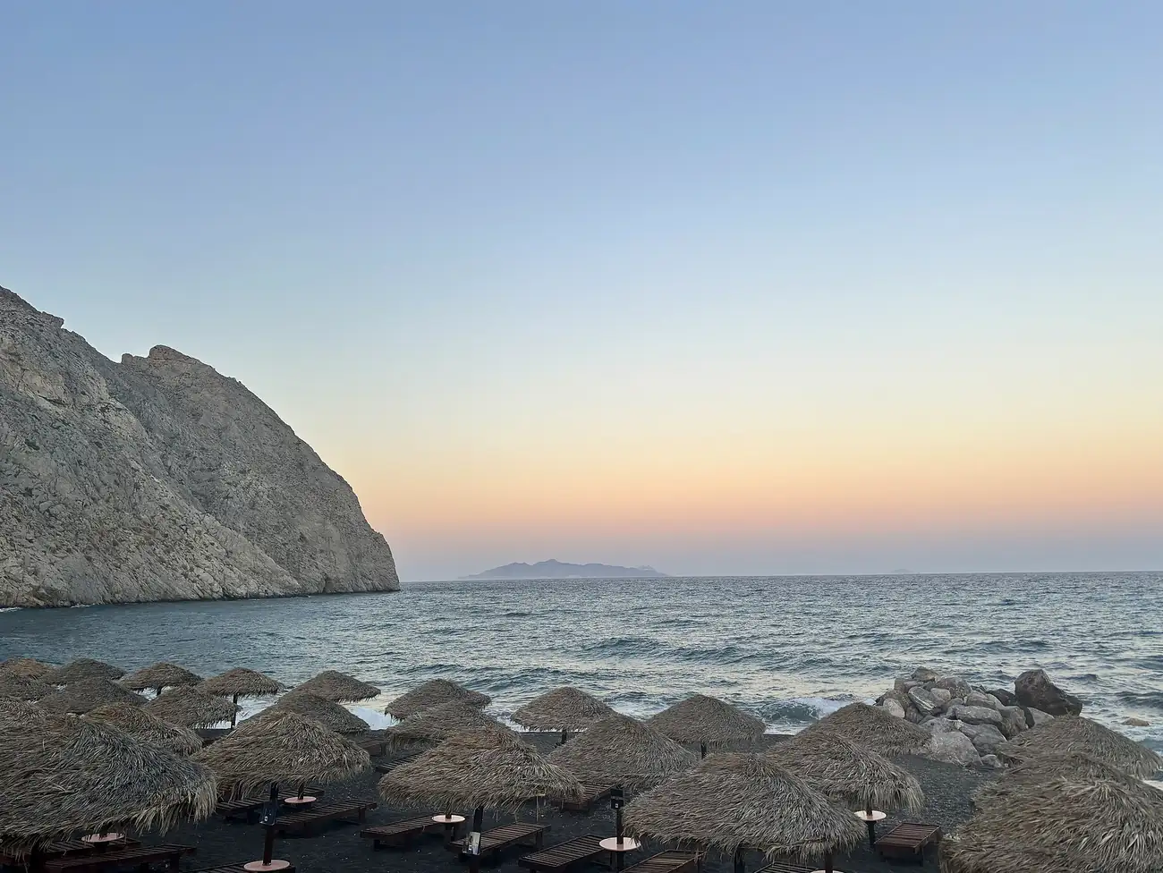 Playa de Perissa en Santorini al atardecer, con sombrillas de paja y la montaña Mesa Vouno