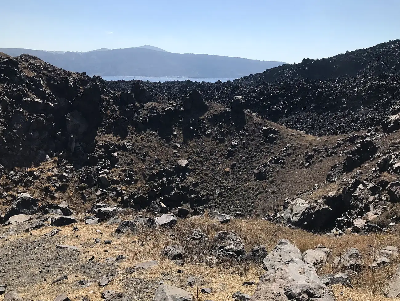 Cráter de lava negra del volcán de Nea Kameni con la caldera de Santorini al fondo